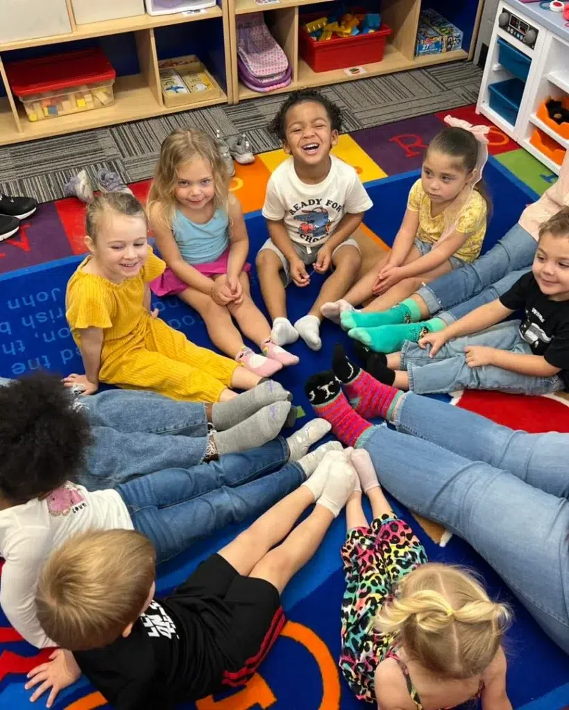 Group of young children sitting on the carpet, smiling, with colorful socks.